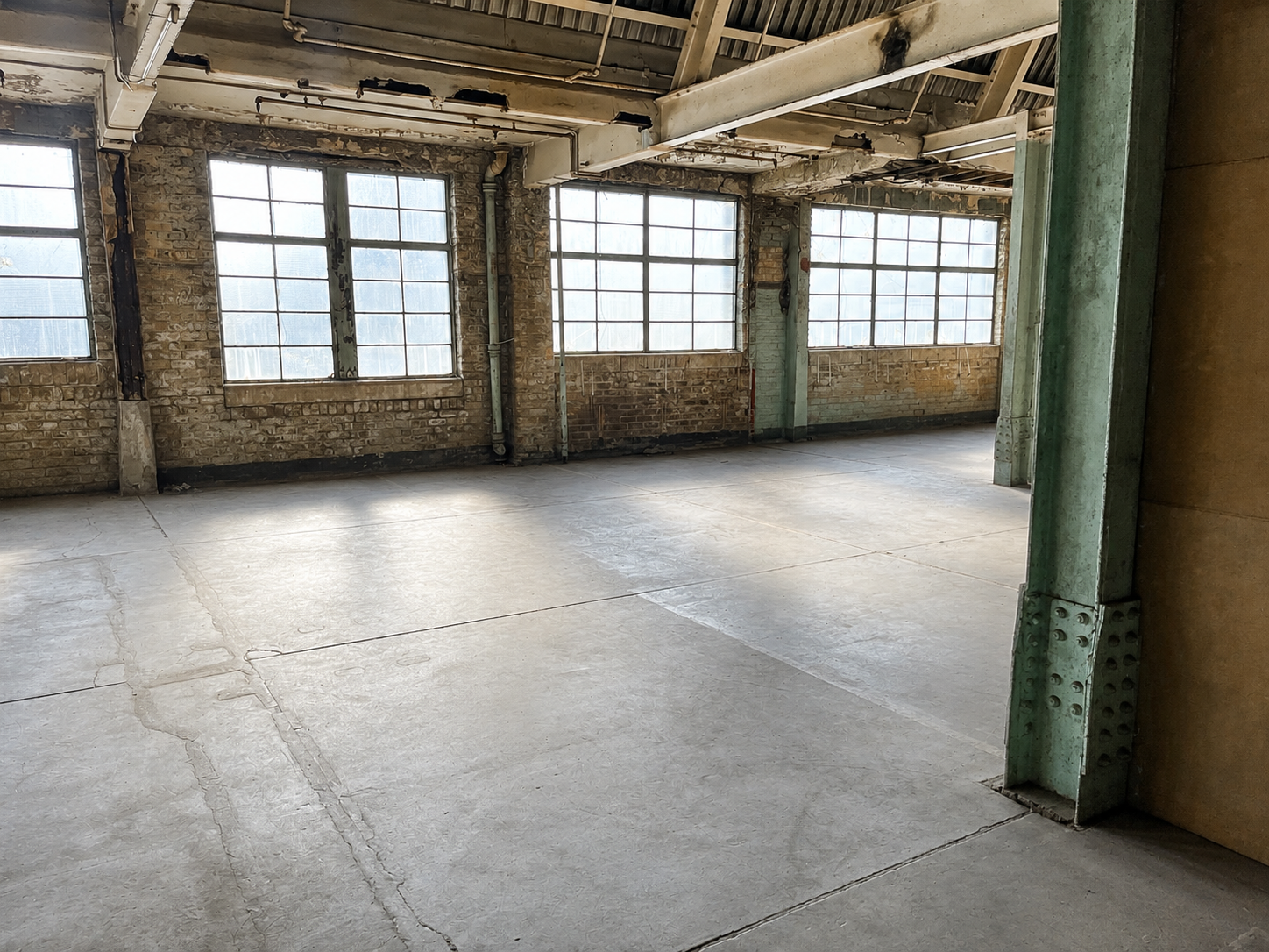 Open industrial studio with tall windows, exposed beams and green steel columns