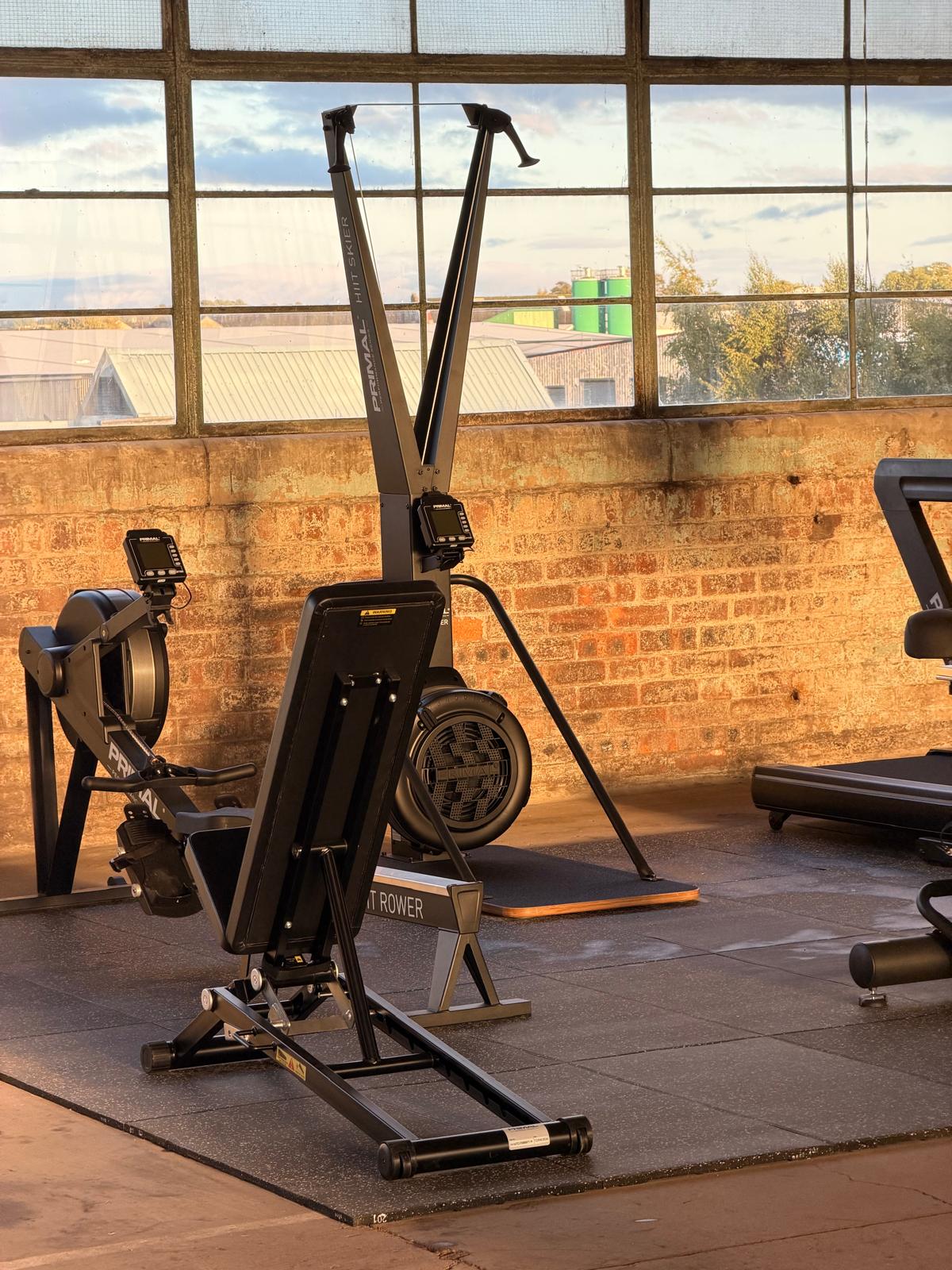 Rowing and ski training machines positioned beside tall factory windows